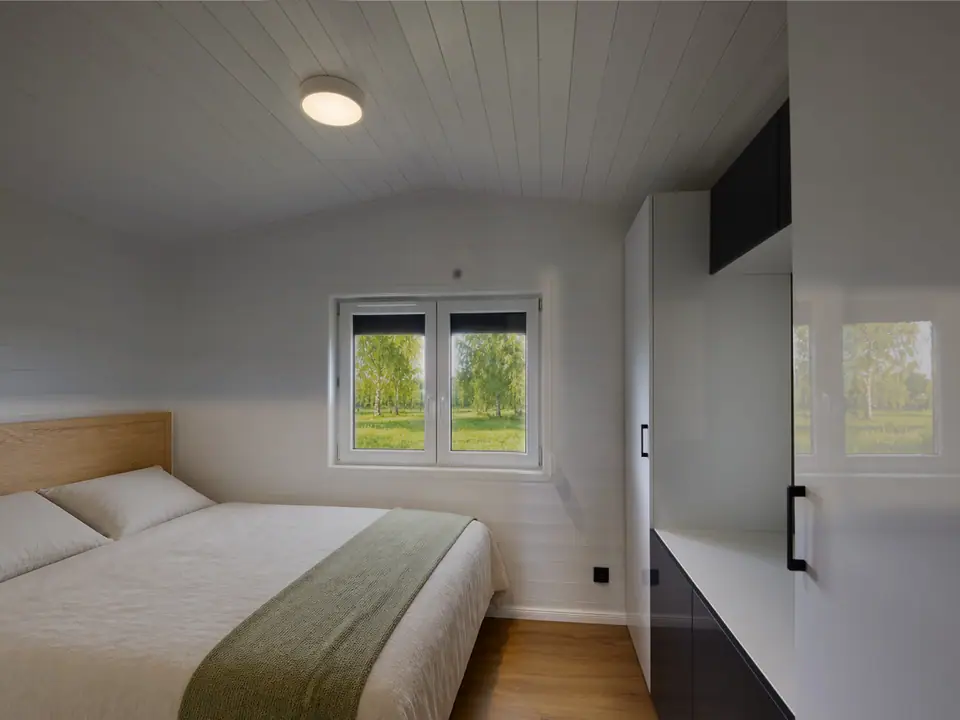 Schlafzimmer mit Doppelbett, hellem Holzkopfteil und weißem Einbauschrank, am Fenster Blick auf Birken und Wiese. Visualisierung