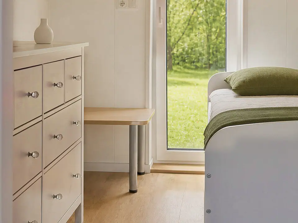Schlafzimmer mit heller Kommode, Bett und einer Fenstertür mit Blick auf die Wiese. Visualisierung
